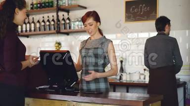 漂亮的现代咖啡馆的礼貌微笑的员工在出售外卖饮料，而快乐的顾客则在付钱